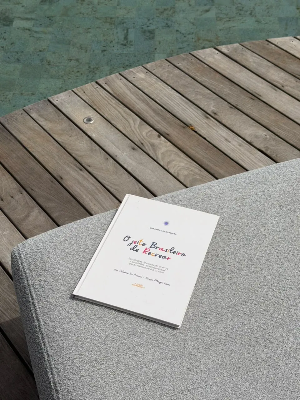 O livro sobre uma espreguiçadeira, com o deck e a piscina ao fundo